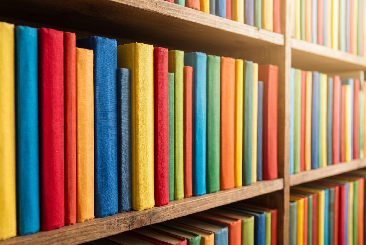 Nahaufnahme bunter Buchrücken in warmem Licht auf Holzregalen