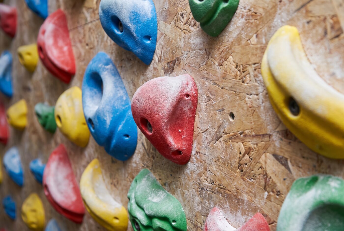 Nahaufnahme bunter Klettergriffe an einer strukturierten Boulderwand mit Chalk-Staub