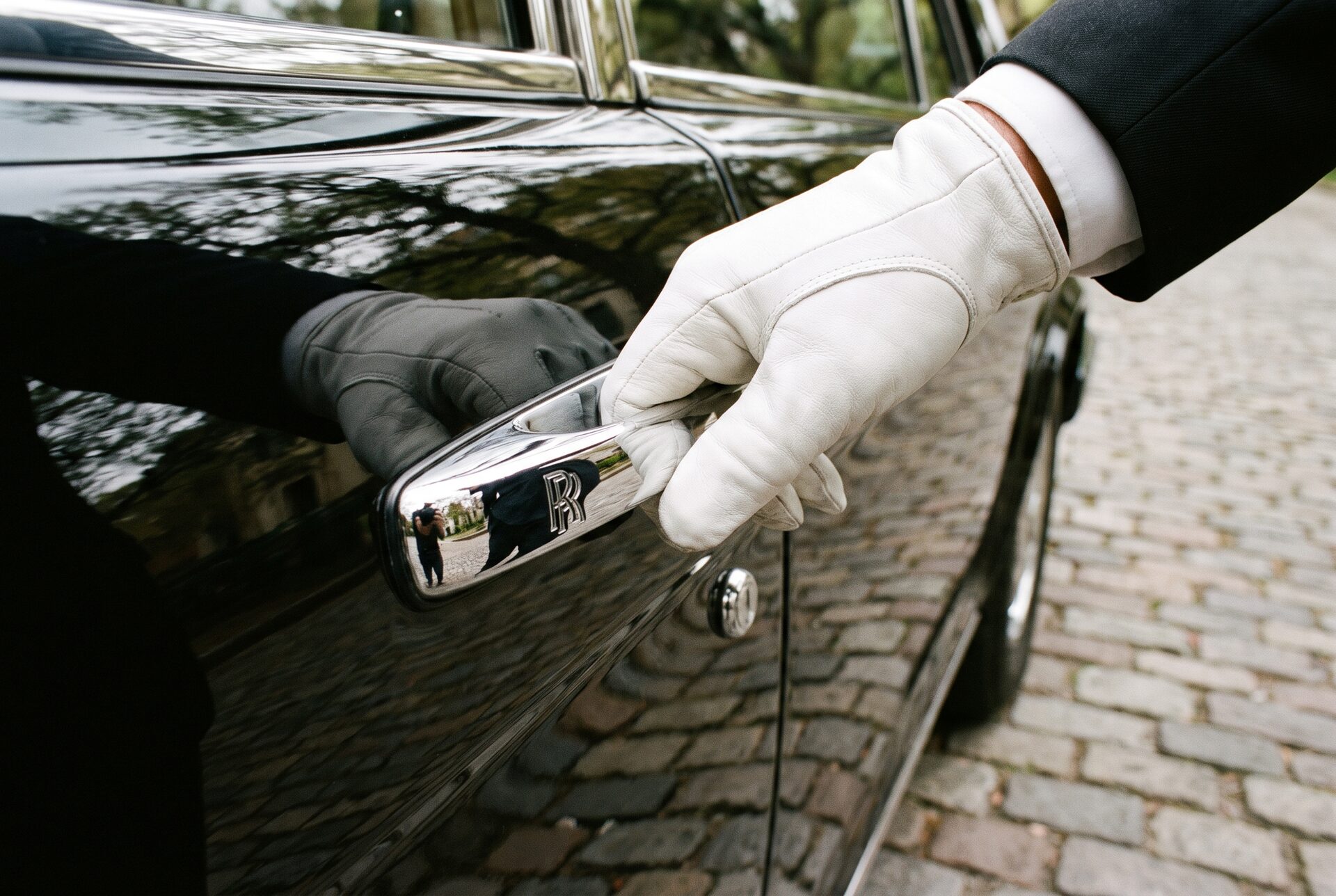 Nahaufnahme einer behandschuhten Hand am polierten Türgriff einer Limousine