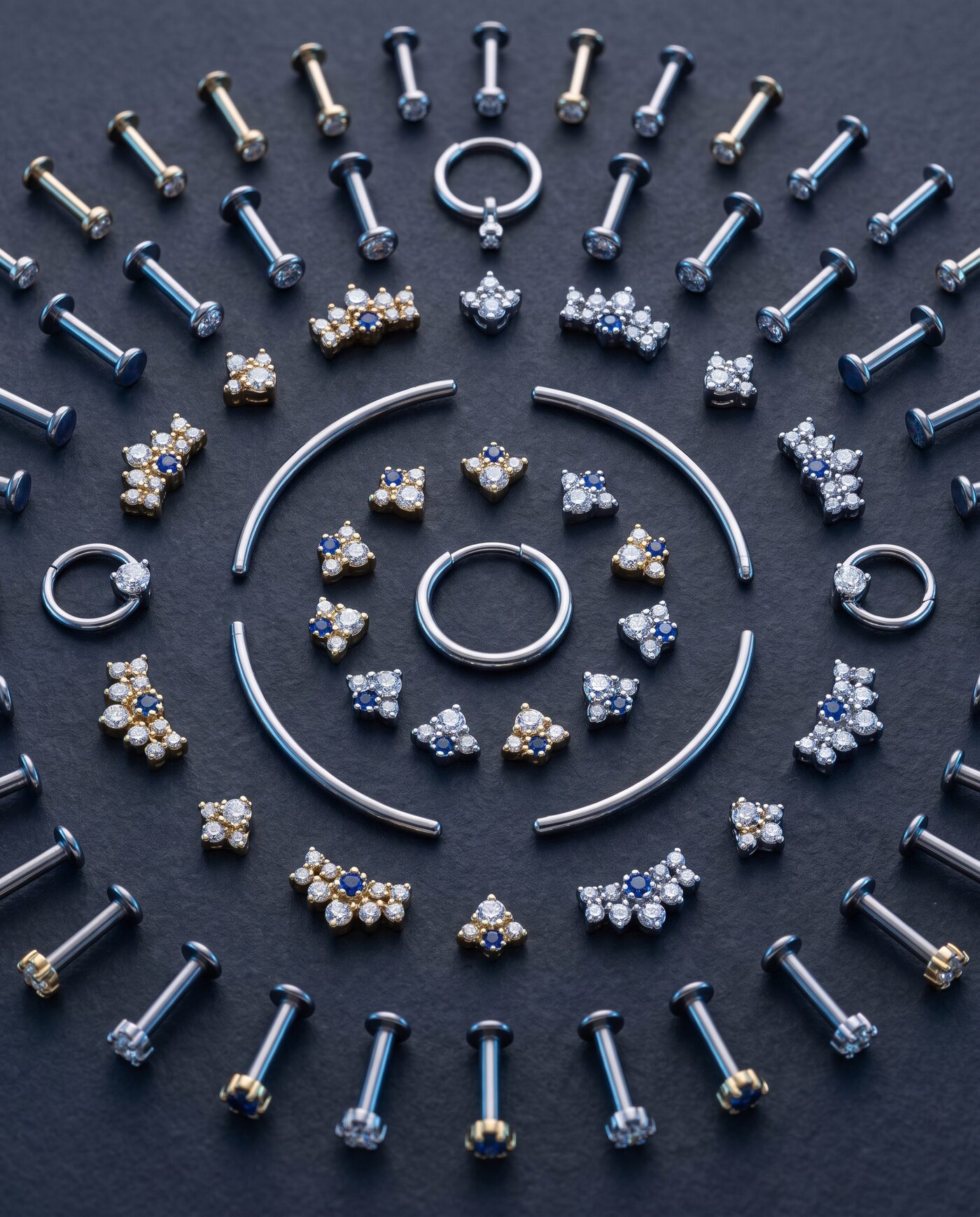 Flatlay mit feinem Piercing-Schmuck aus Titan und Gold auf dunklem Grund