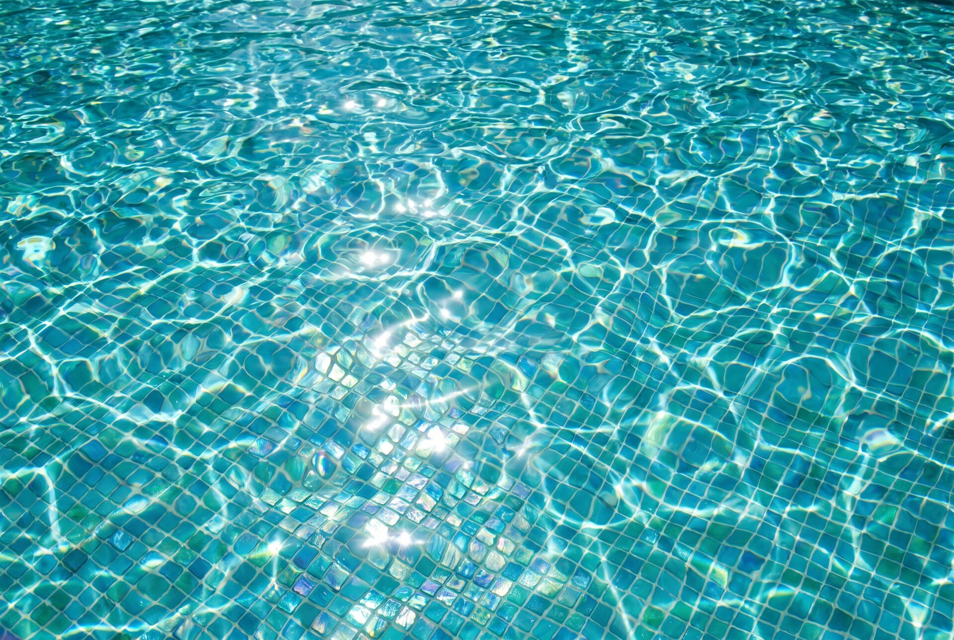 Sonnenbeschienene türkise Wasseroberfläche mit Lichtmustern auf Mosaikfliesen